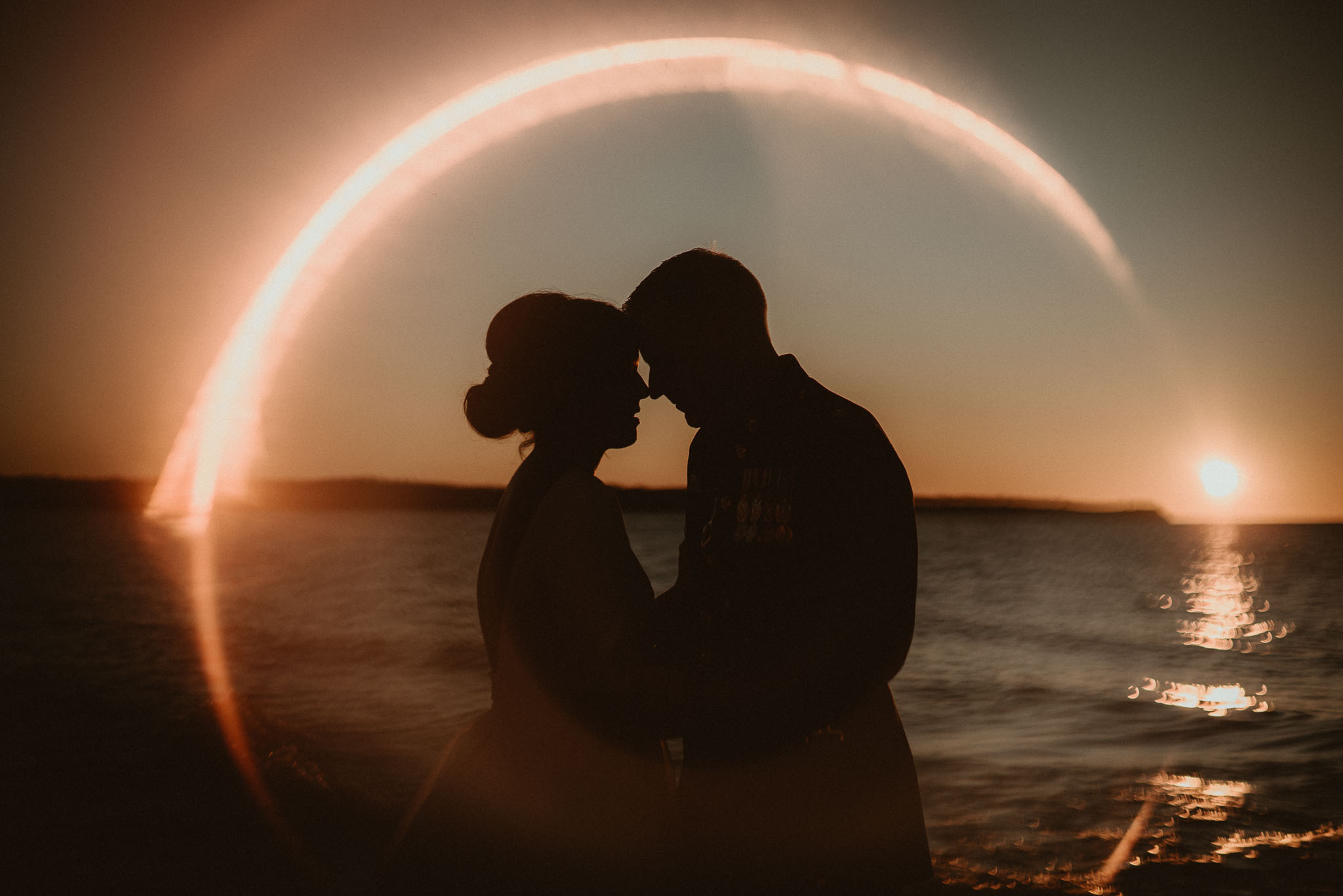 The bride and groom silhouetted inside sunset ring of fire.