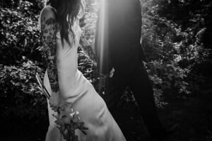 Black and white photo of a couple walking walking, holding hands, with the focus on the brides tatoos.