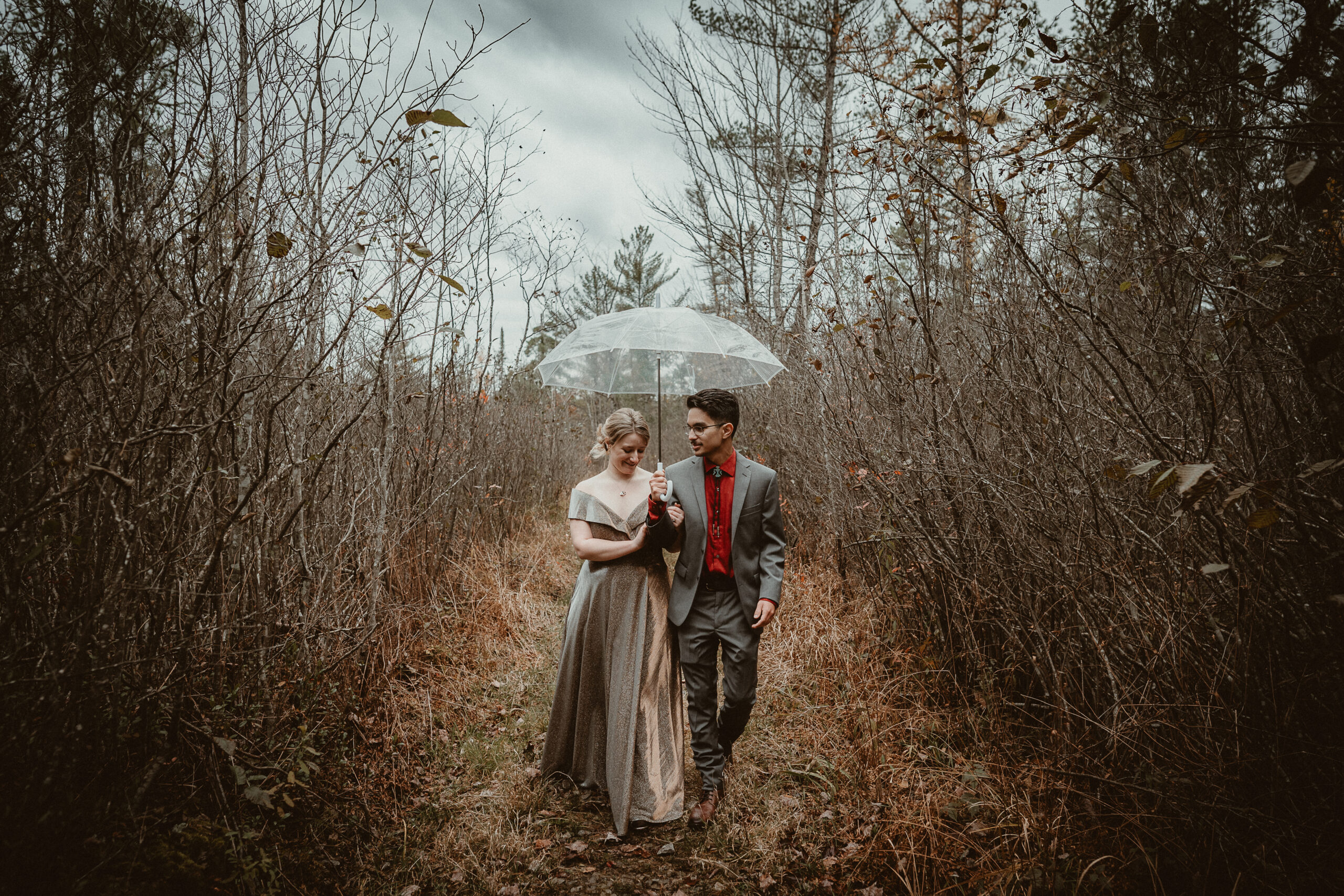 Bride and Groom walking in the woods in the rain with a clear umbrella.
