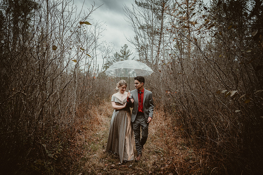Bride and Groom walking in the woods in the rain with a clear umbrella after eloping at Hartwick Pines.