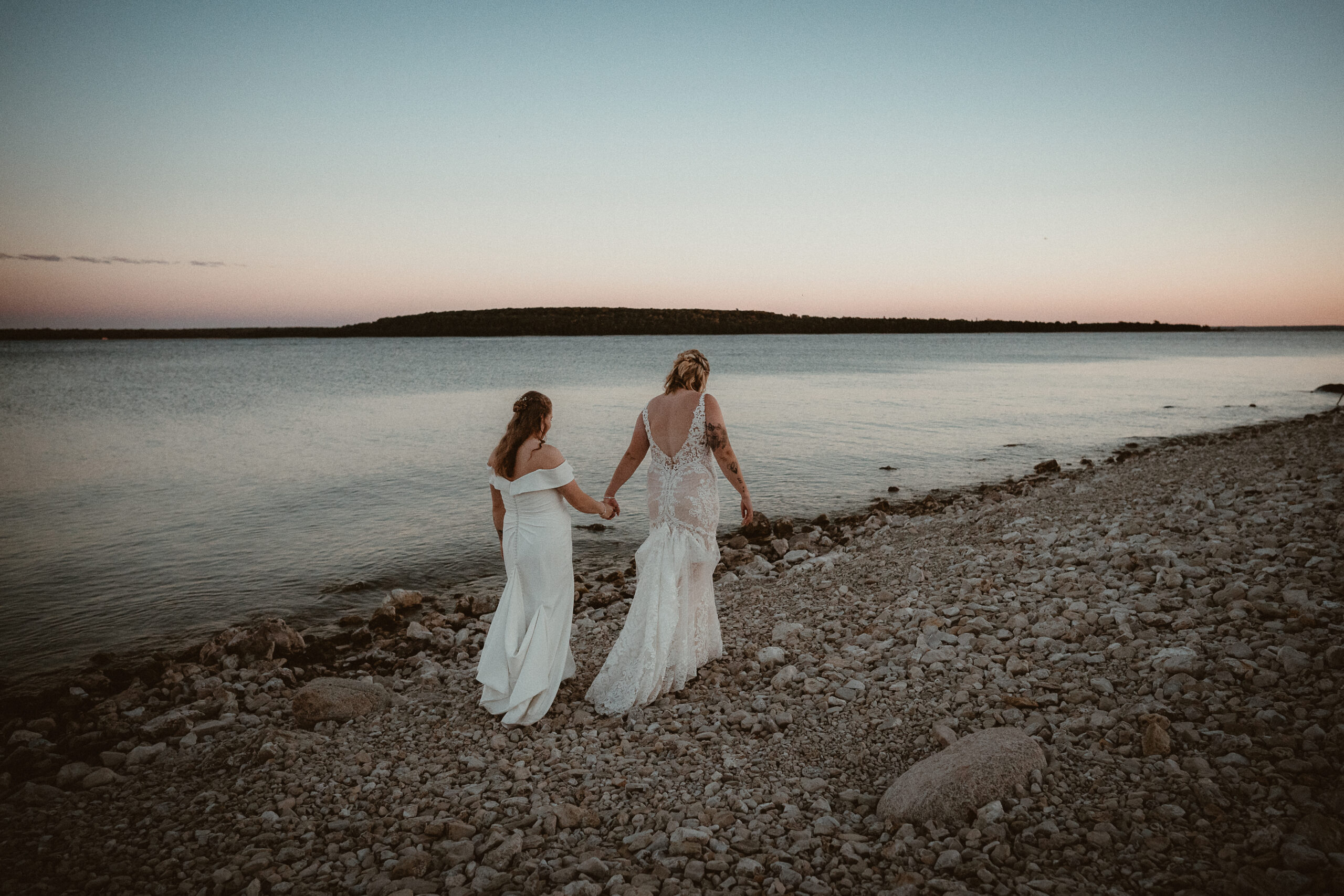 Brides walking holding hands along Lake Huron at sunset.