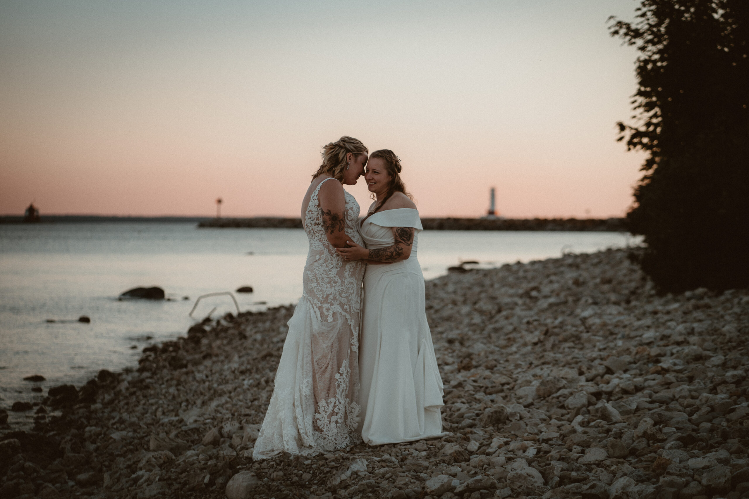 Brides holding one another at sunset on the rocky beach of lake Huron.