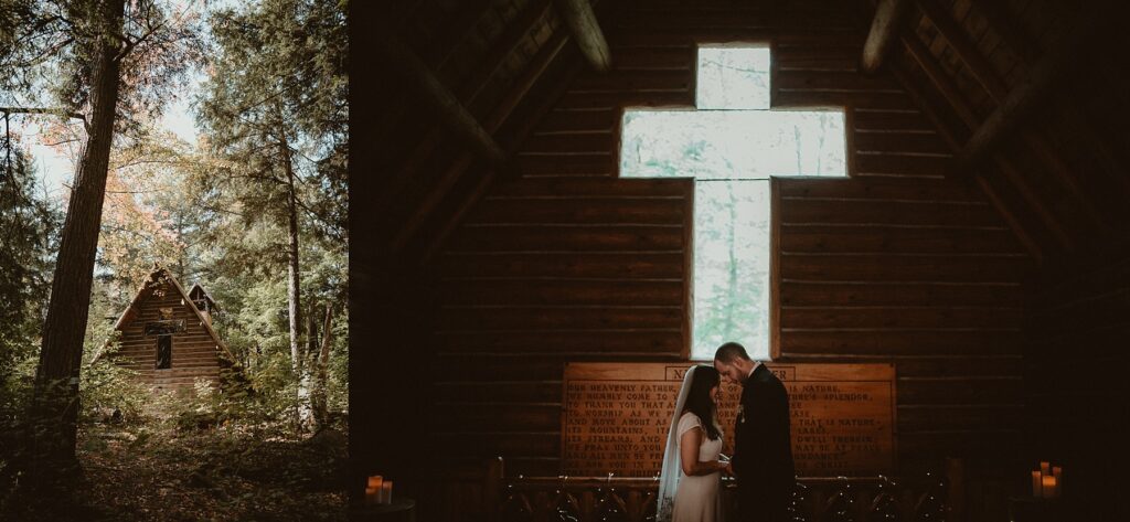 Couple standing together in a small log chapel with cross shaped window behind them.