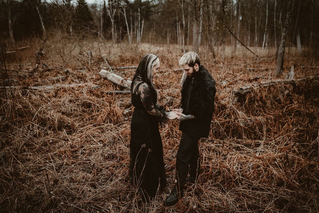 Couple in black wedding clothes standing together holding hands in the woods.