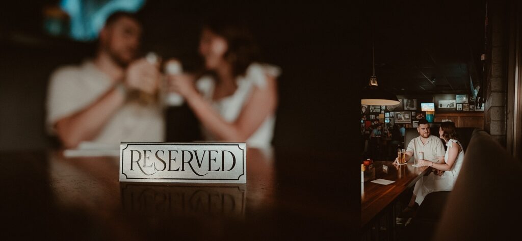 Couple sitting in VIP booth, toasting drinks in background, with the reserved sign in focus at their favorite bar.