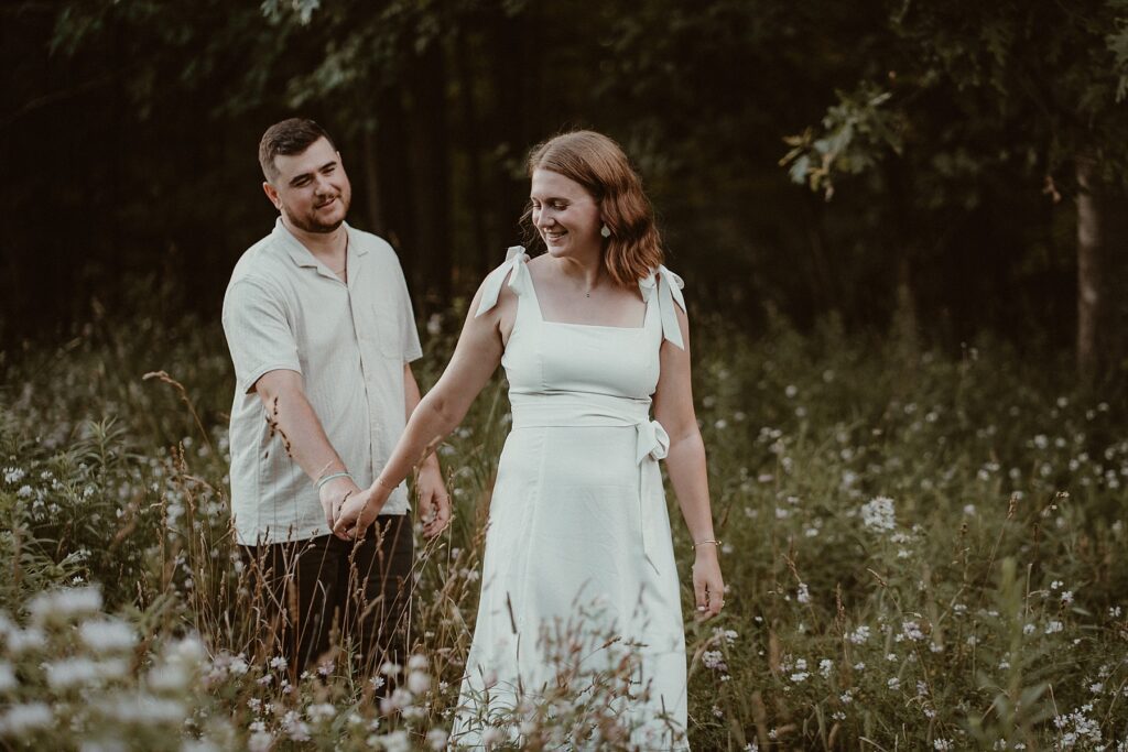 Couple walking through a field of wildflowers while she looks back on him.