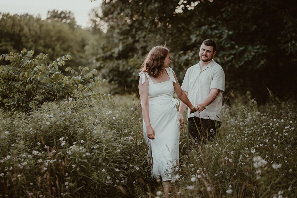 Couple walking through a field of wildflowers while she looks back on him.