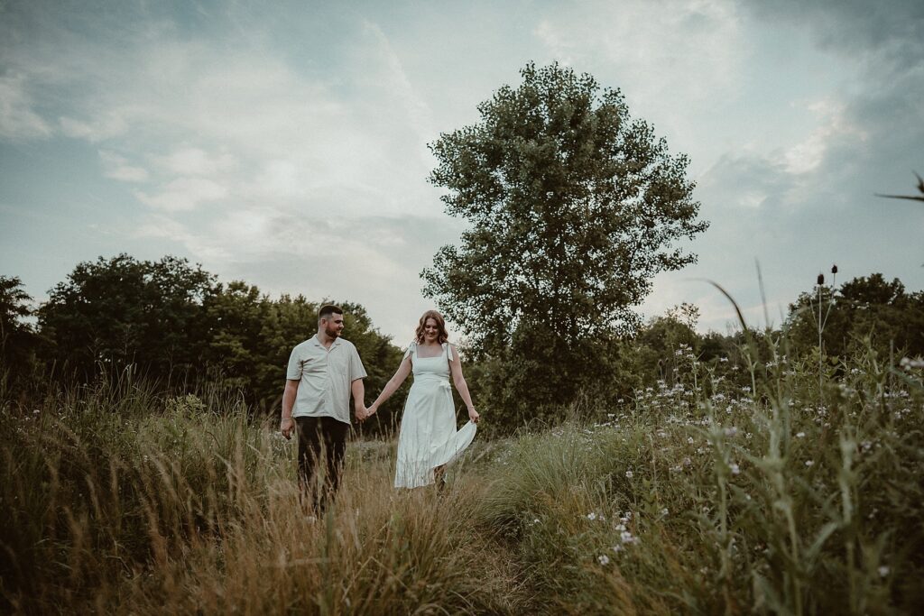 Couple walking down a hill of wildflowers holding hands.