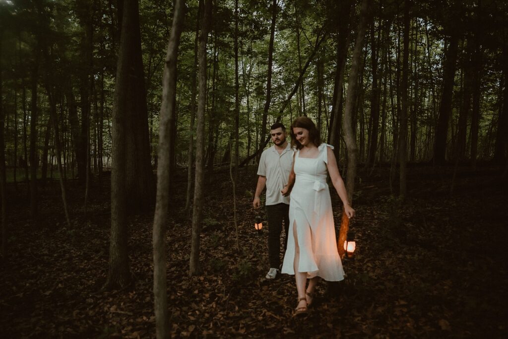 Couple walking with lit lanterns through a dark forest area.