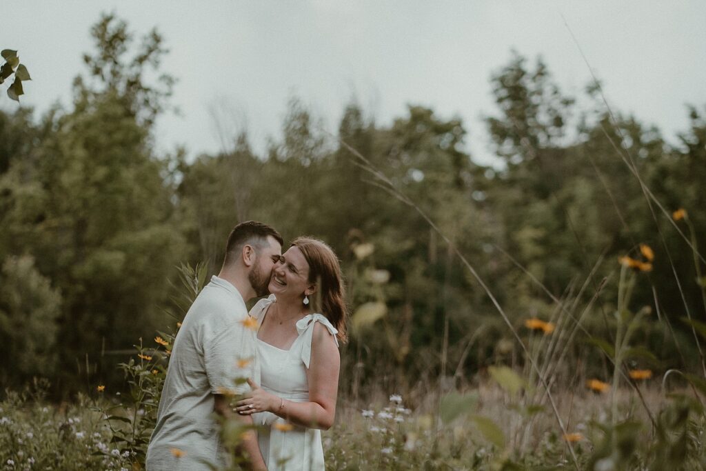 Couple together laughing in a field of wildflowers.