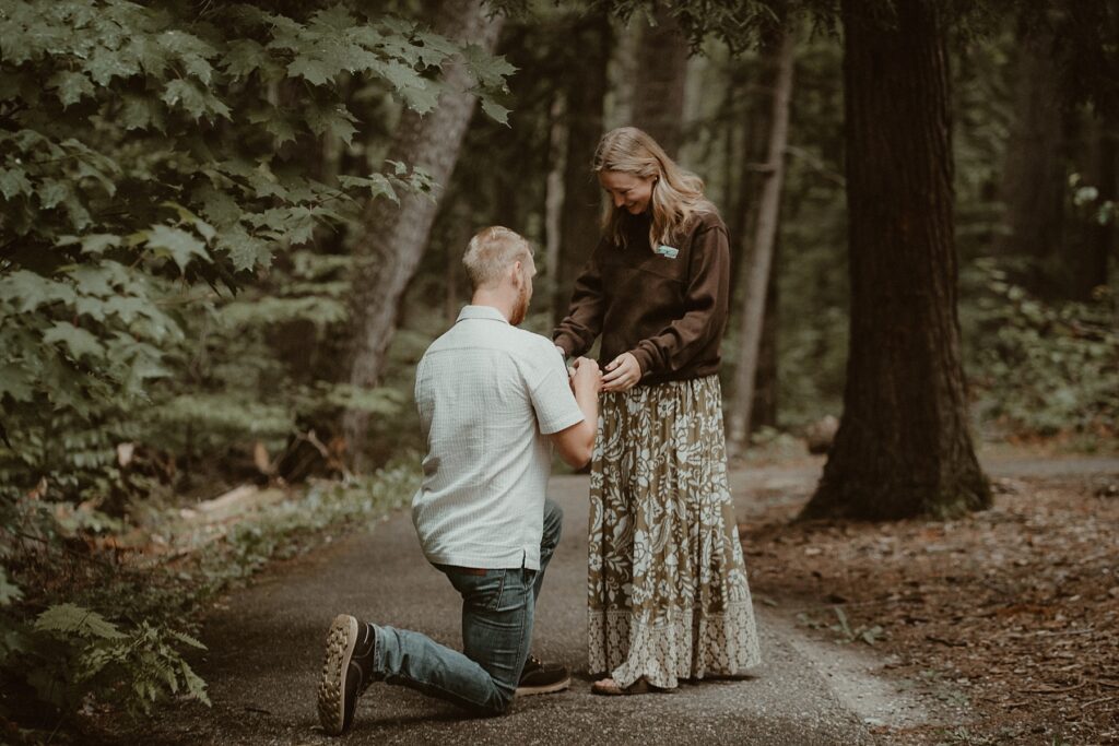 Guy on one knee placing the engagement ring on his girlfriends finger.