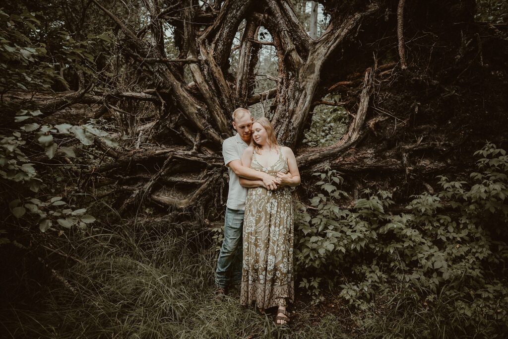Him holding her from behind in front of an uprooted tree.
