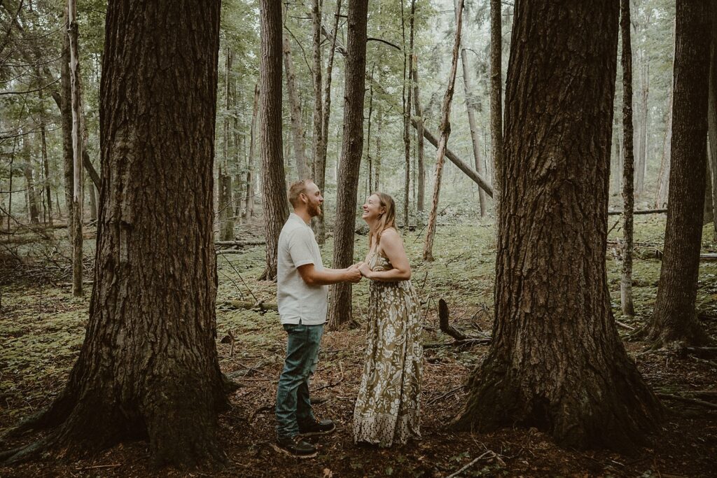 Couple standing in the rainy woods laughing together.