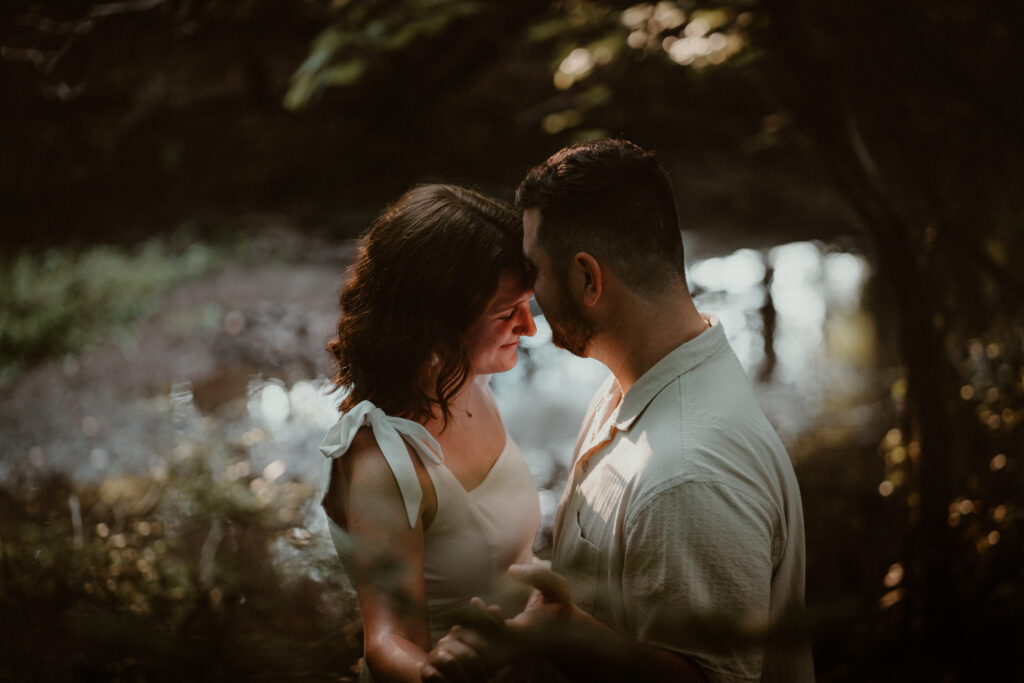 Couple holding each other near the river with the sun lighting their faces.