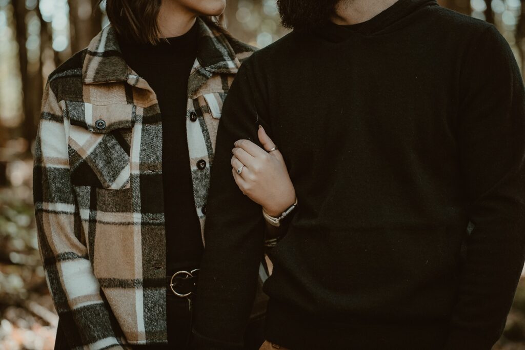 Close up of engagement ring on her hand while holding his arm.