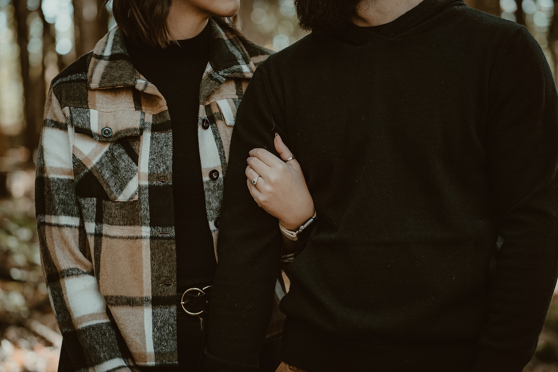 Close up of engagement ring on her hand while holding his arm.
