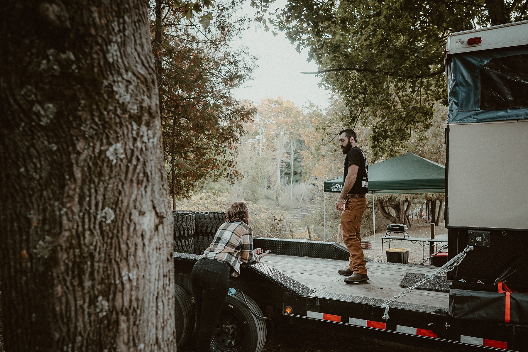 Engaged couple setting up their campsite in Frankfort, Michigan with fall foliage in the background.