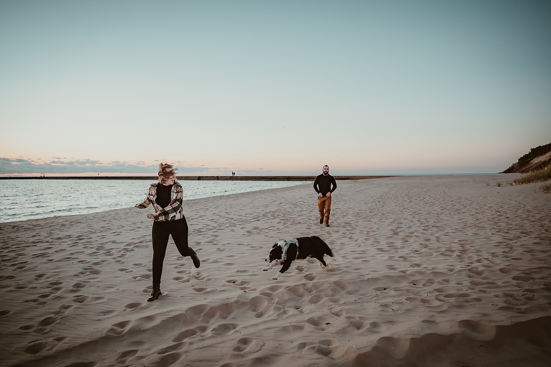 Border Collie chasing couple along the shoreline during a Frankfort, Michigan engagement session.