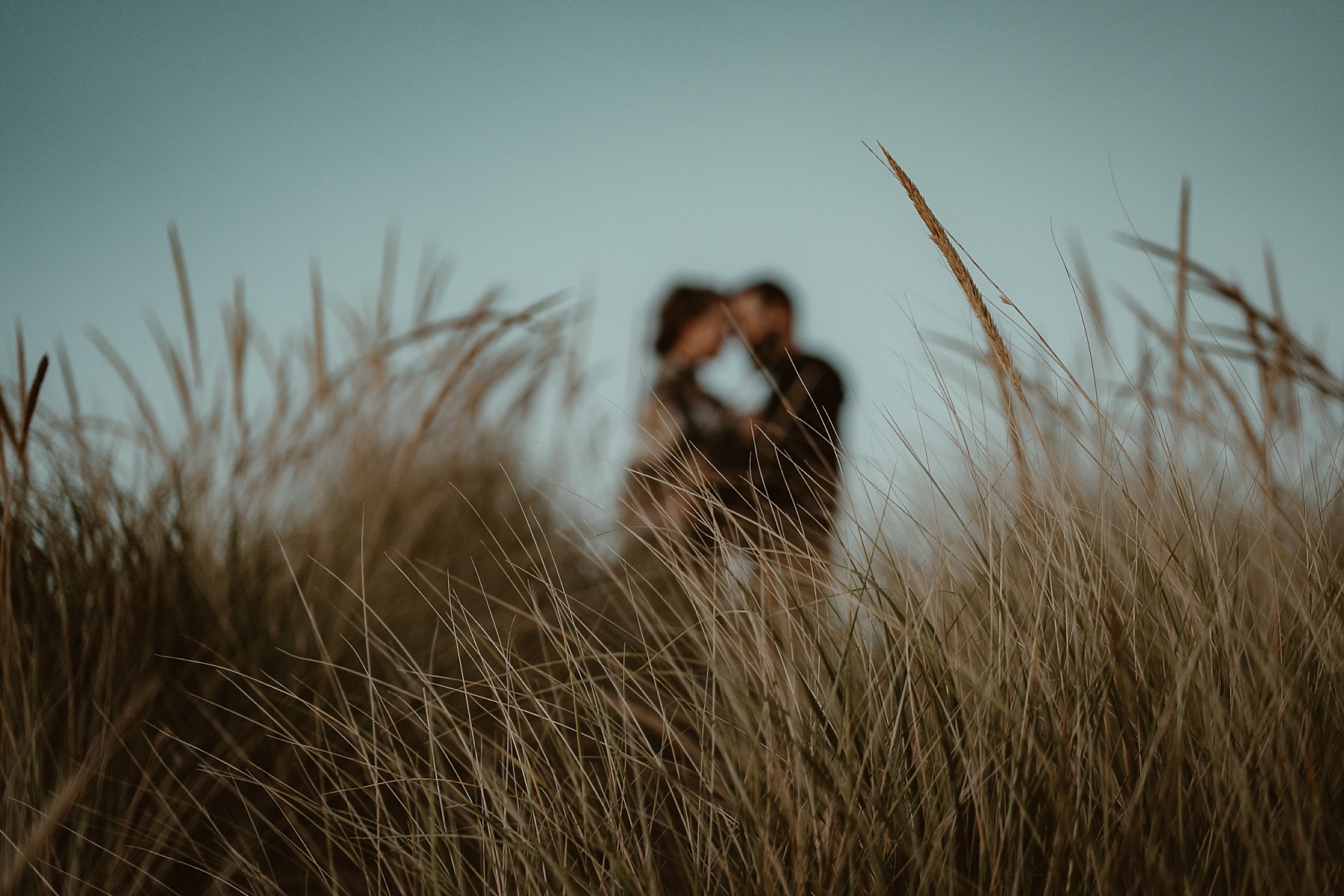 Couple holding each other at top of small sand dune at engagement session on Lake Michigan.