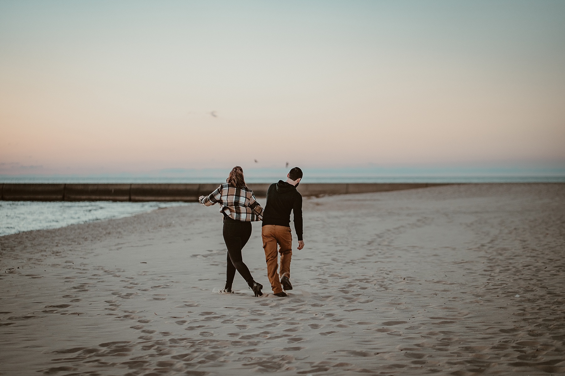 Couple playfully walking along the shoreline during a Frankfort, Michigan engagement session.
