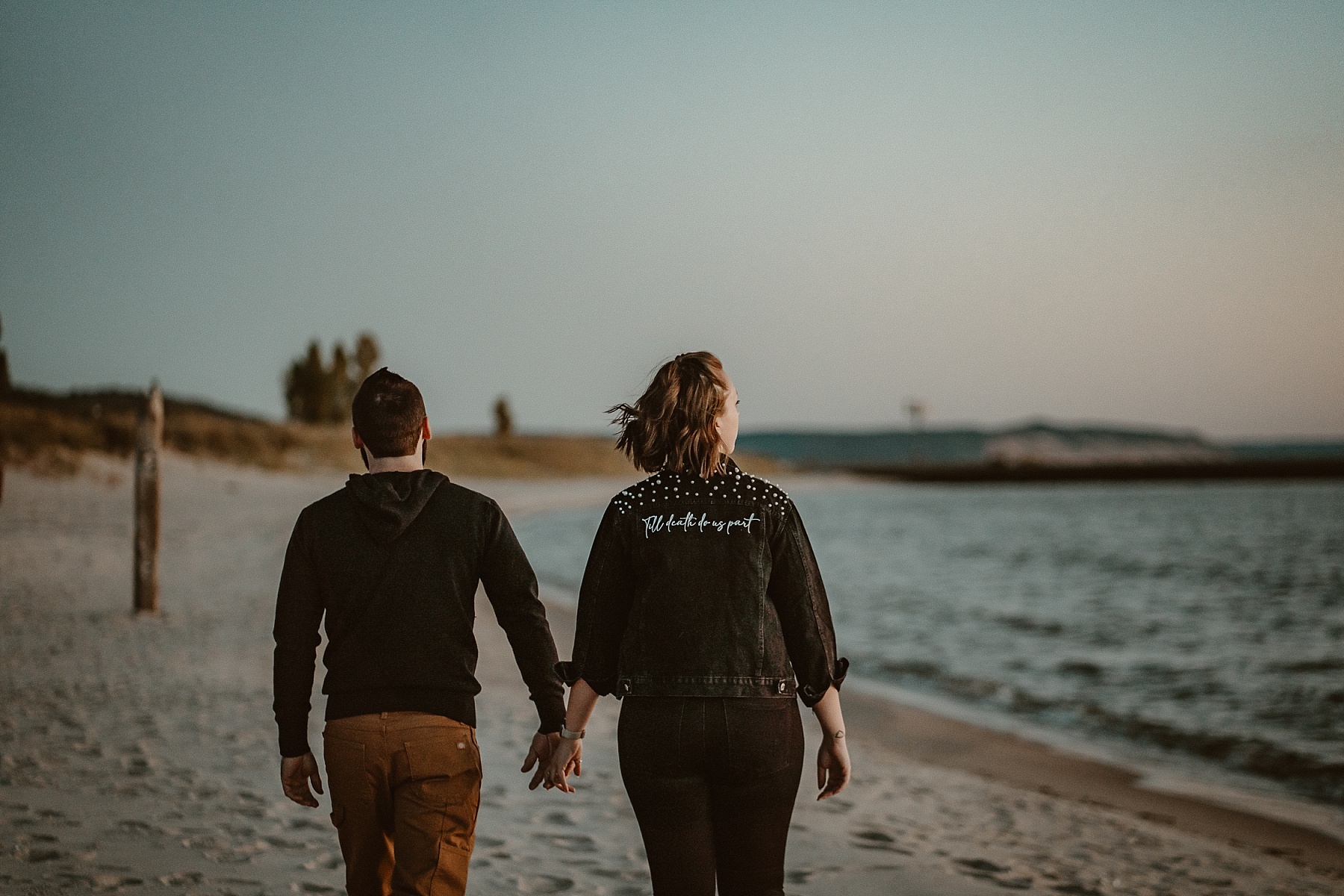 Couple holding hands during a Lake Michigan sunset with pastel skies and waves rolling in.