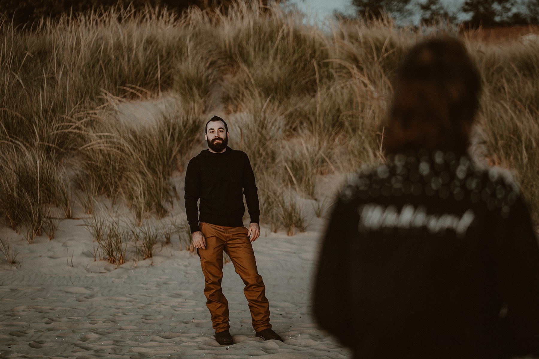 Girl with black jean jacket that says Till Death Do Us Part on the back in foreground with guy in background on the beach of Lake Michigan.