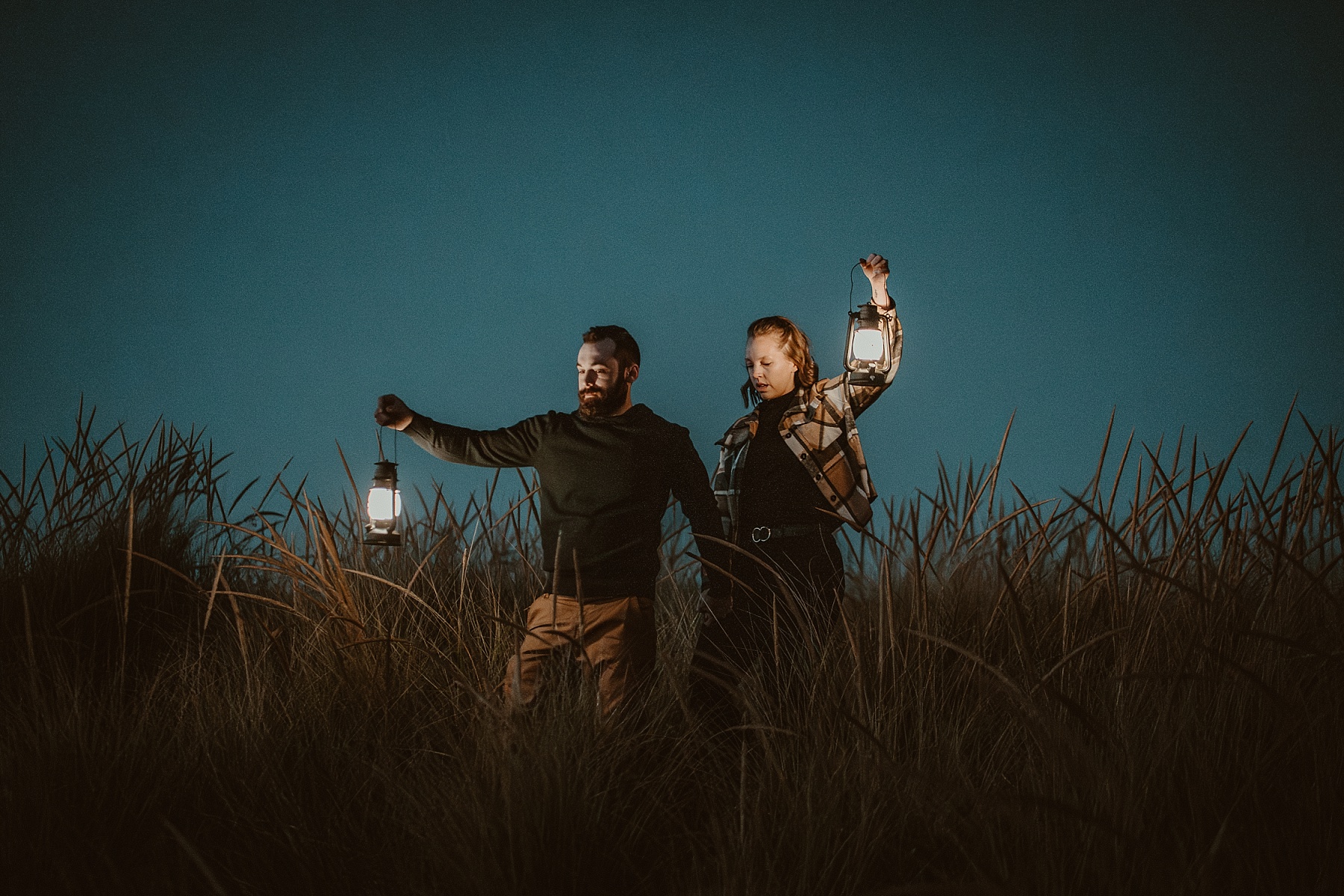 Couple holding hands carrying lanterns at blue hour on Lake Michigan.