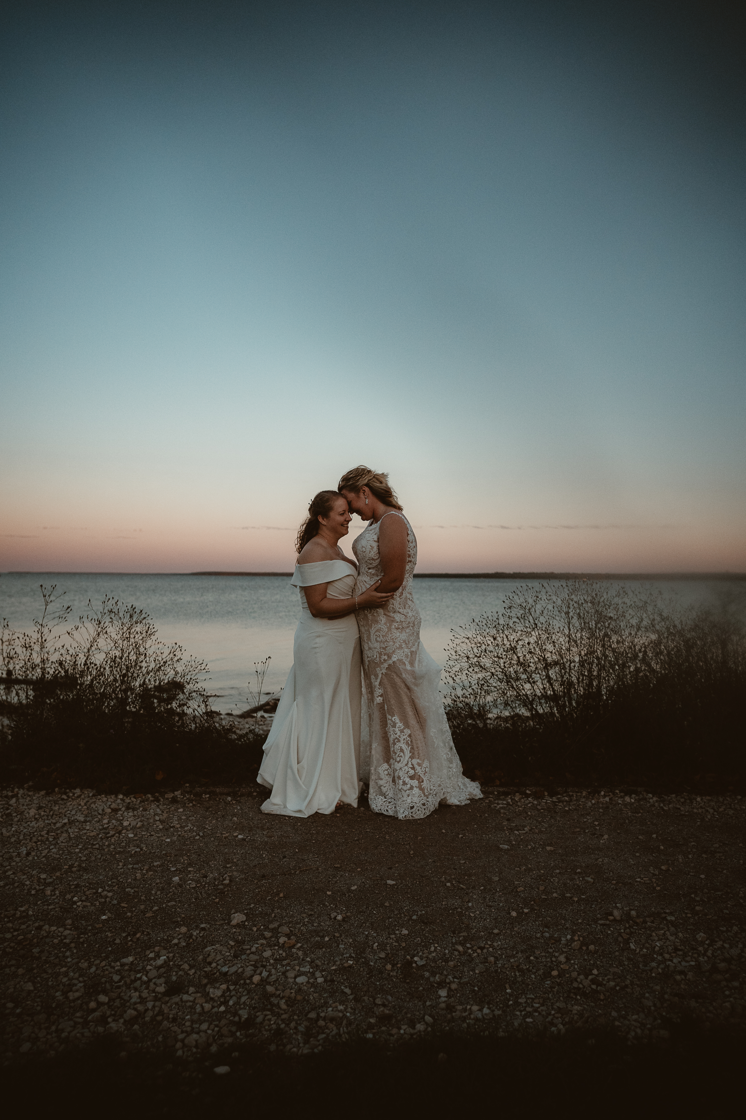 LGBTQ+ brides holding each other on the beach at sunset.
