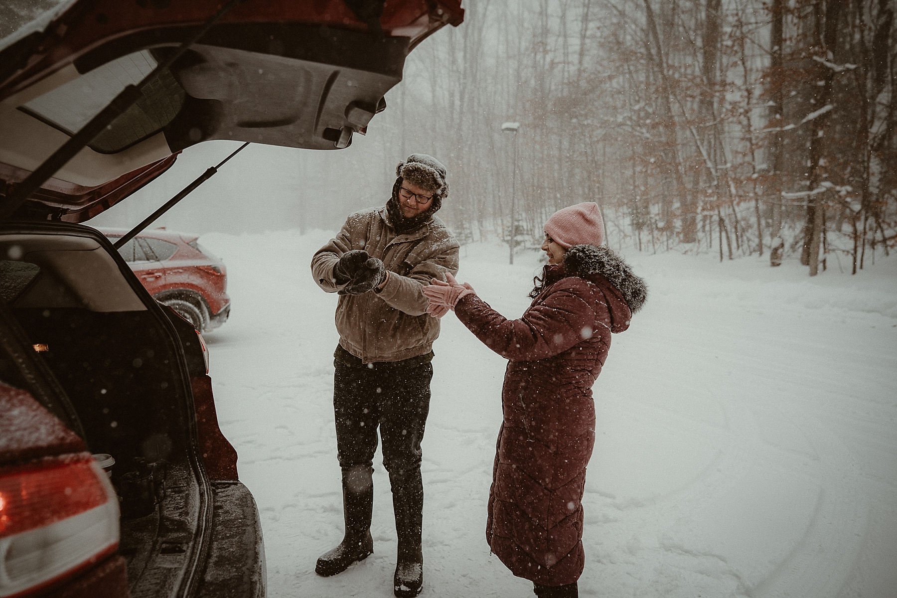 Florida couple bundling up in snowy pine forest during Northern Michigan winter engagement session.