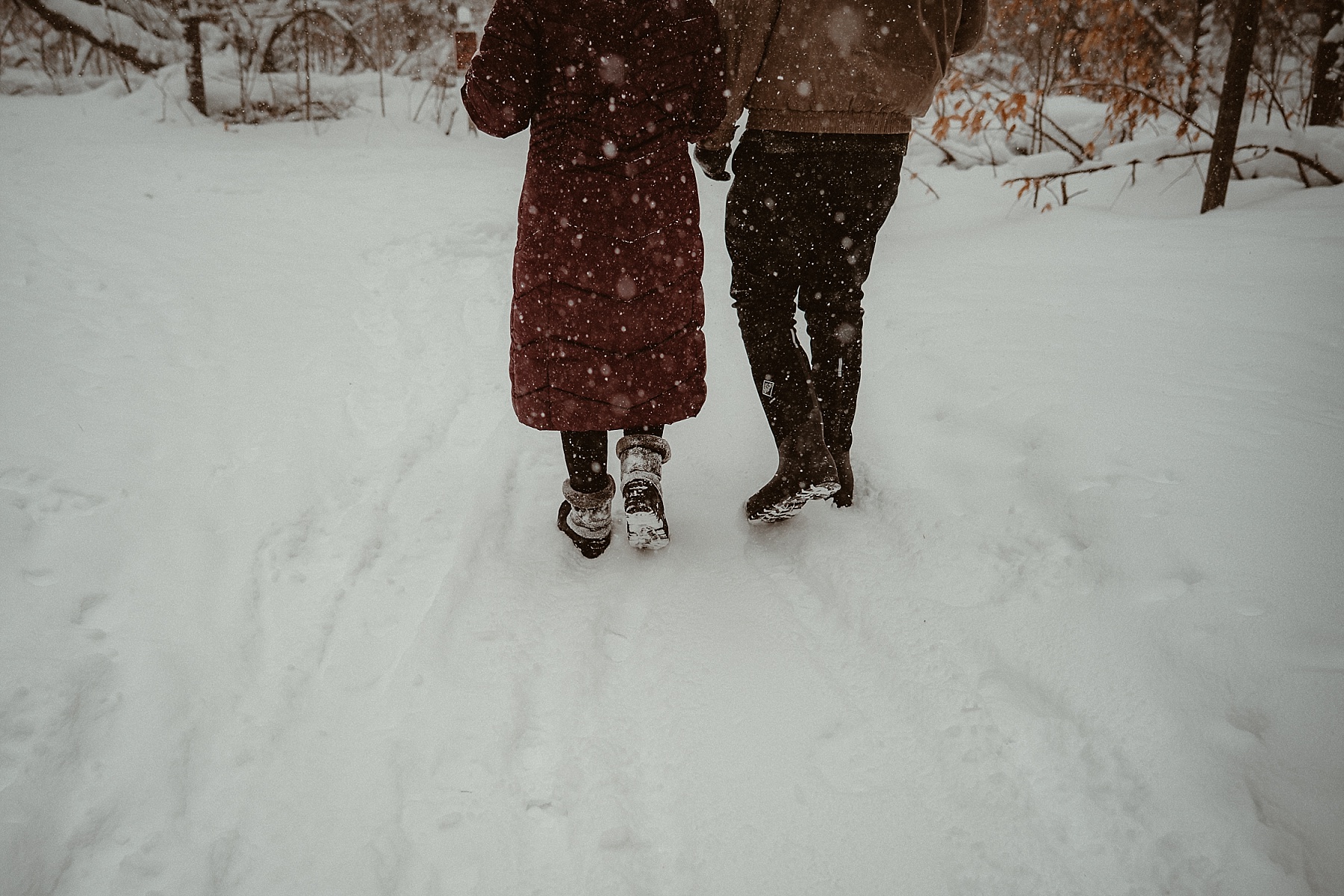 Couple walking through heavy snowfall during winter engagement session at Hartwick Pines State Park in Northern Michigan.