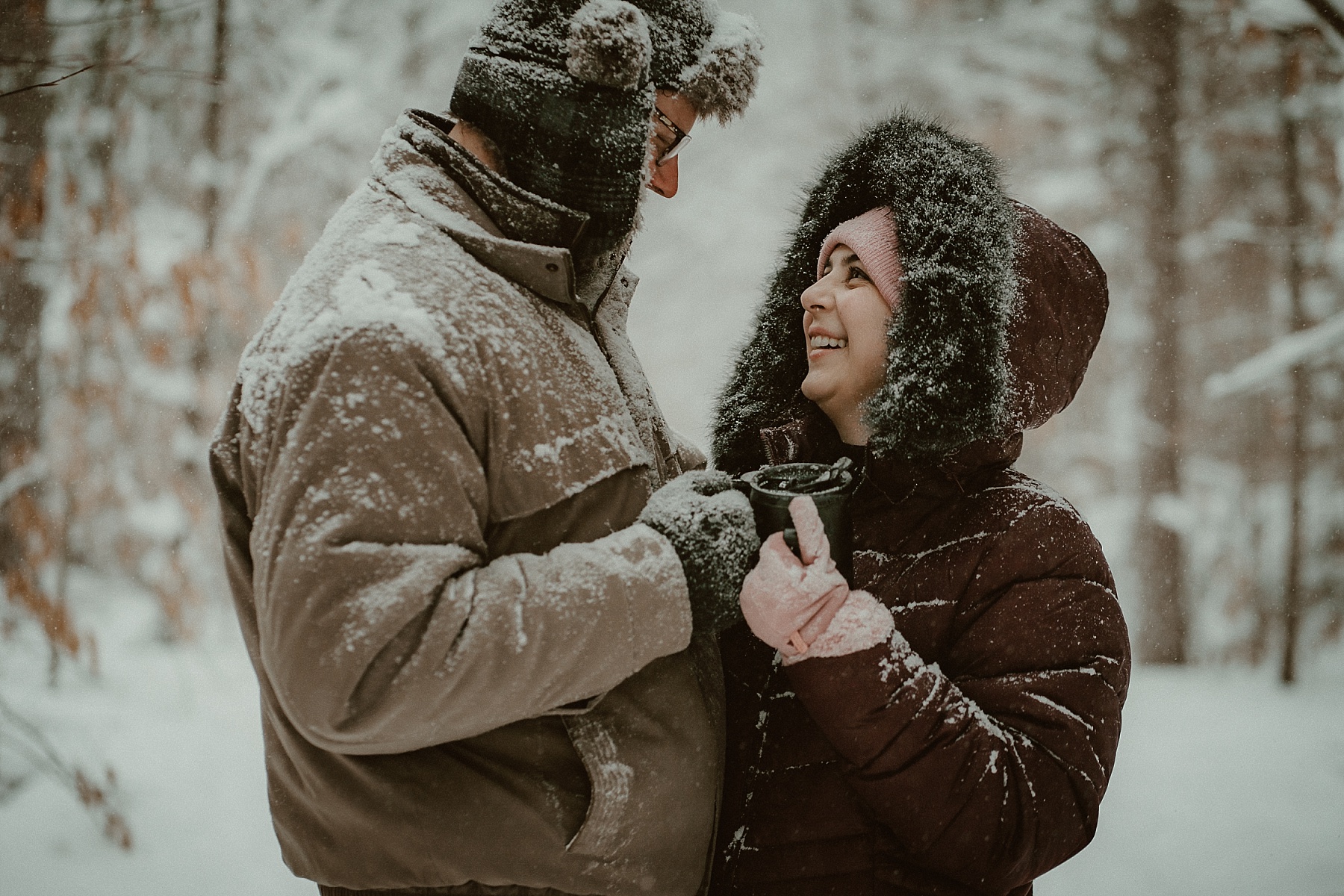 Couple laughing together in deep snow during a cold-weather engagement session in Michigan.