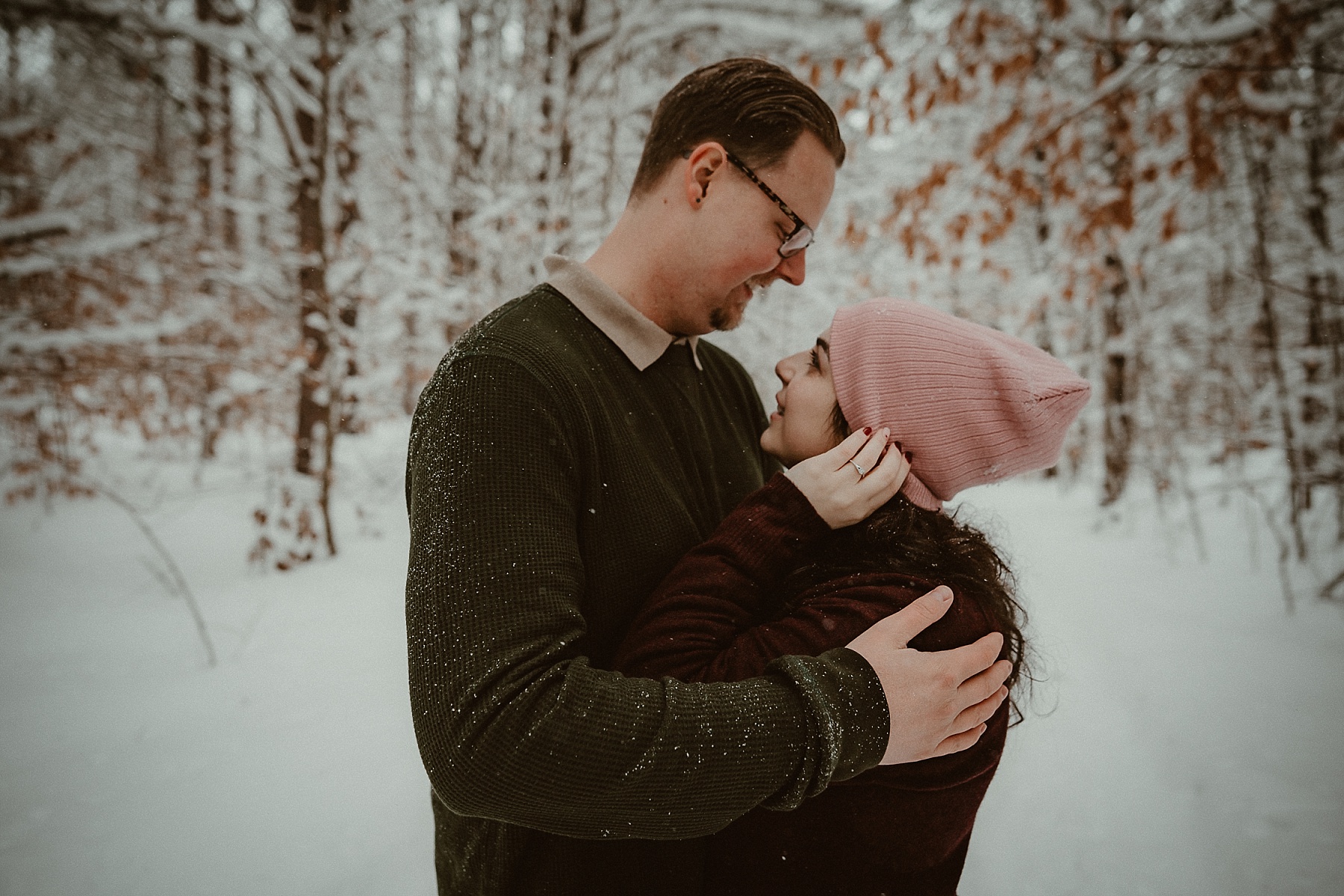 Couple embracing in snowy pine forest during Northern Michigan winter engagement session.