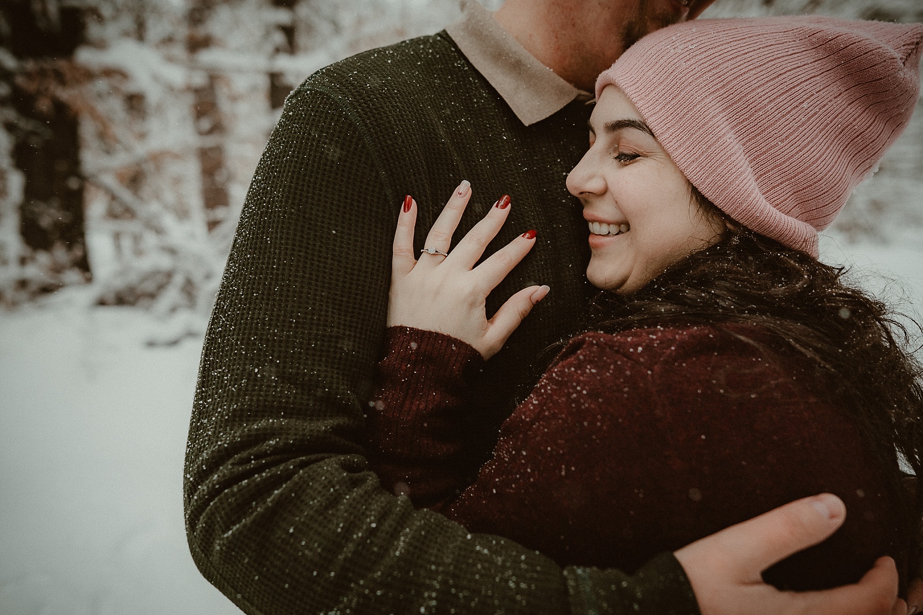 Couple embracing in snowy pine forest during Grayling Michigan winter engagement session.