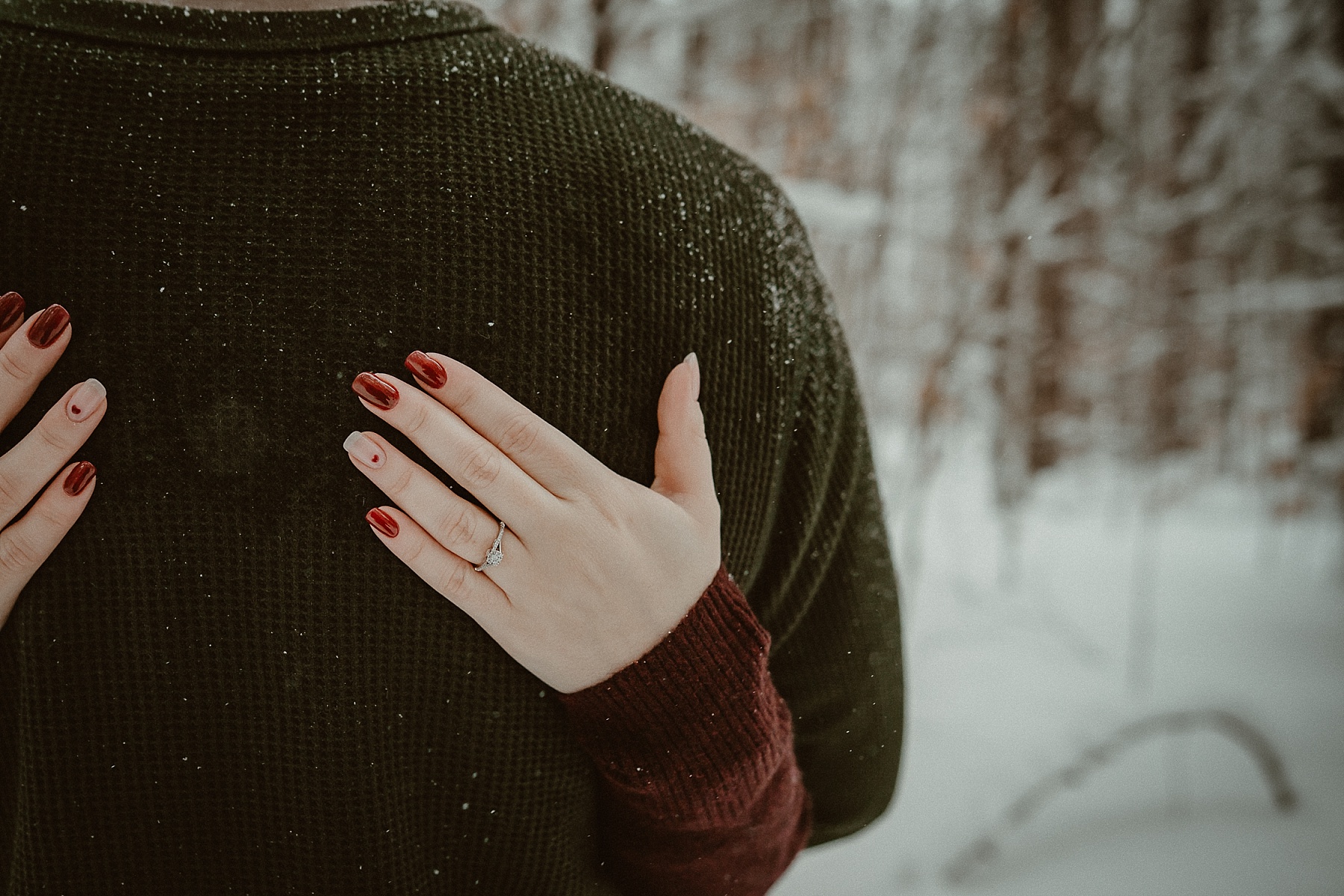 Close up of girls hand with engagement ring on in snowy pine forest during Grayling Michigan winter engagement session.