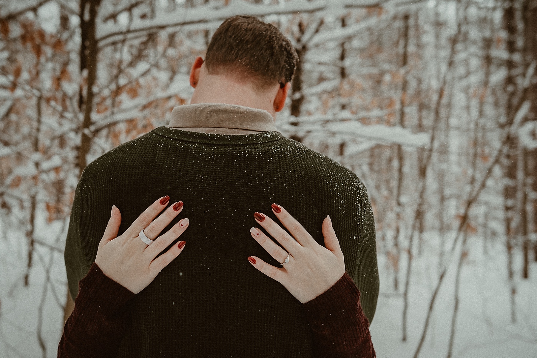 Close up of girls hand with engagement ring on in snowy pine forest during Grayling Michigan winter engagement session.