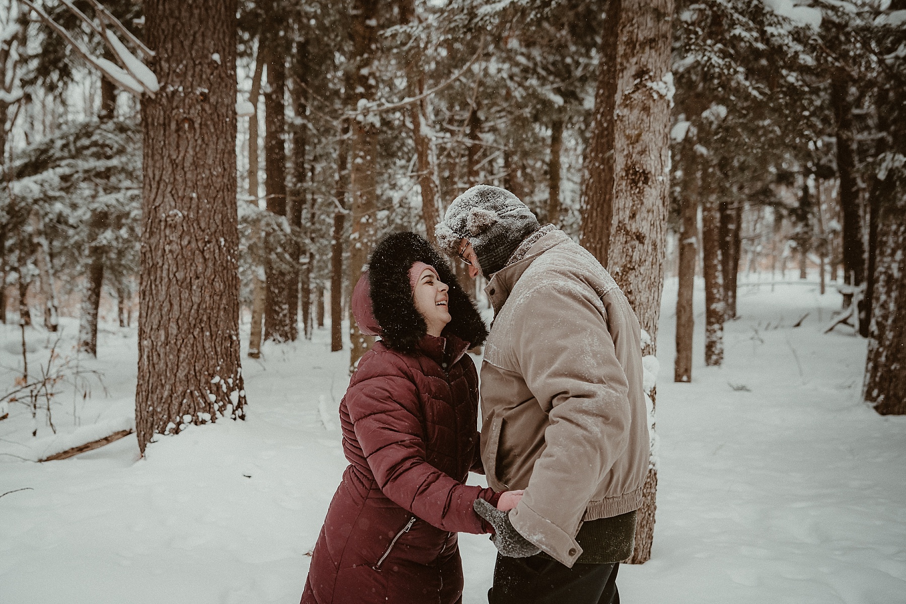 Couple laughing together in deep snow during a cold-weather engagement session in Grayling Michigan.