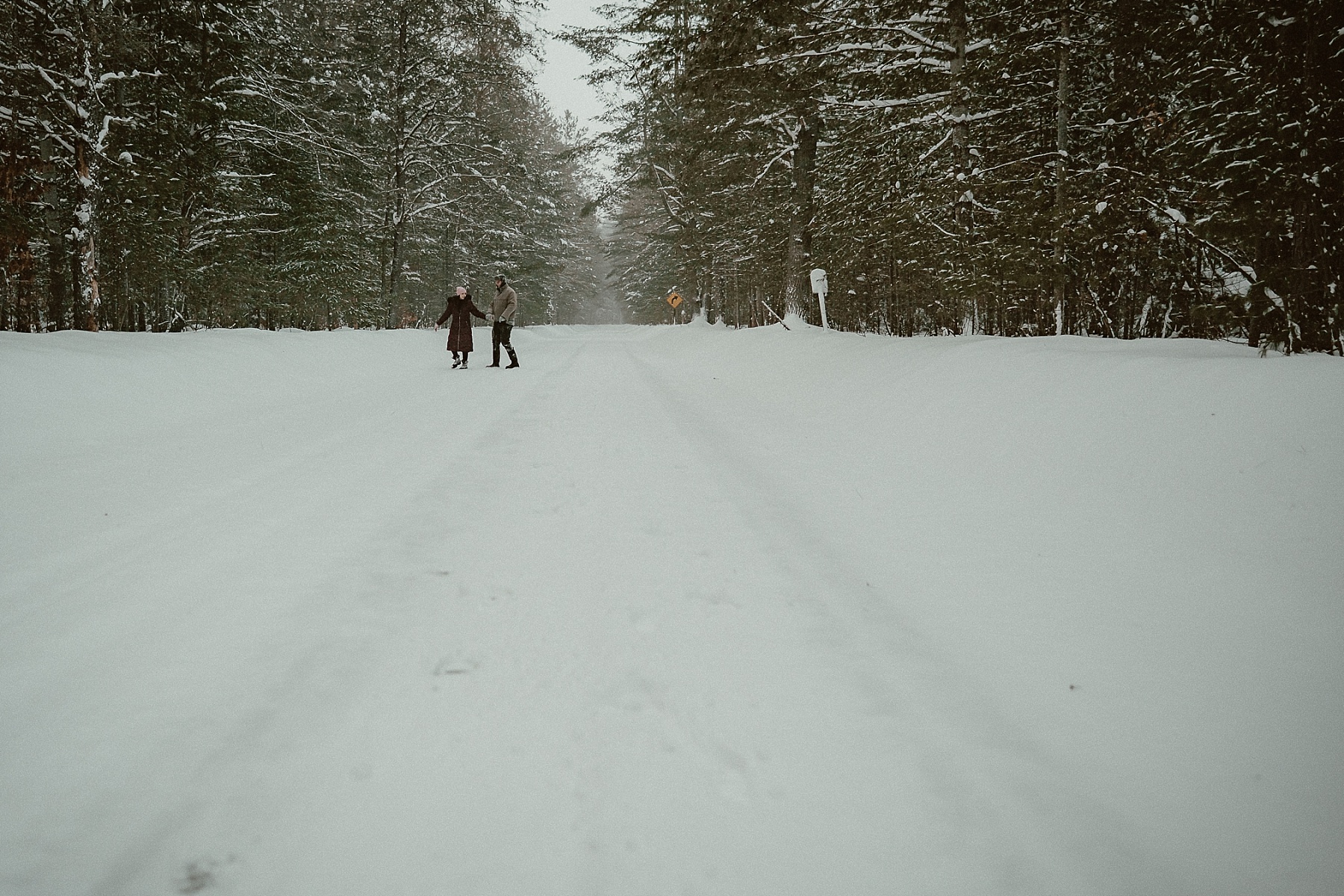 Couple paying in heavy snowfall during winter engagement session at Hartwick Pines State Park in Northern Michigan.