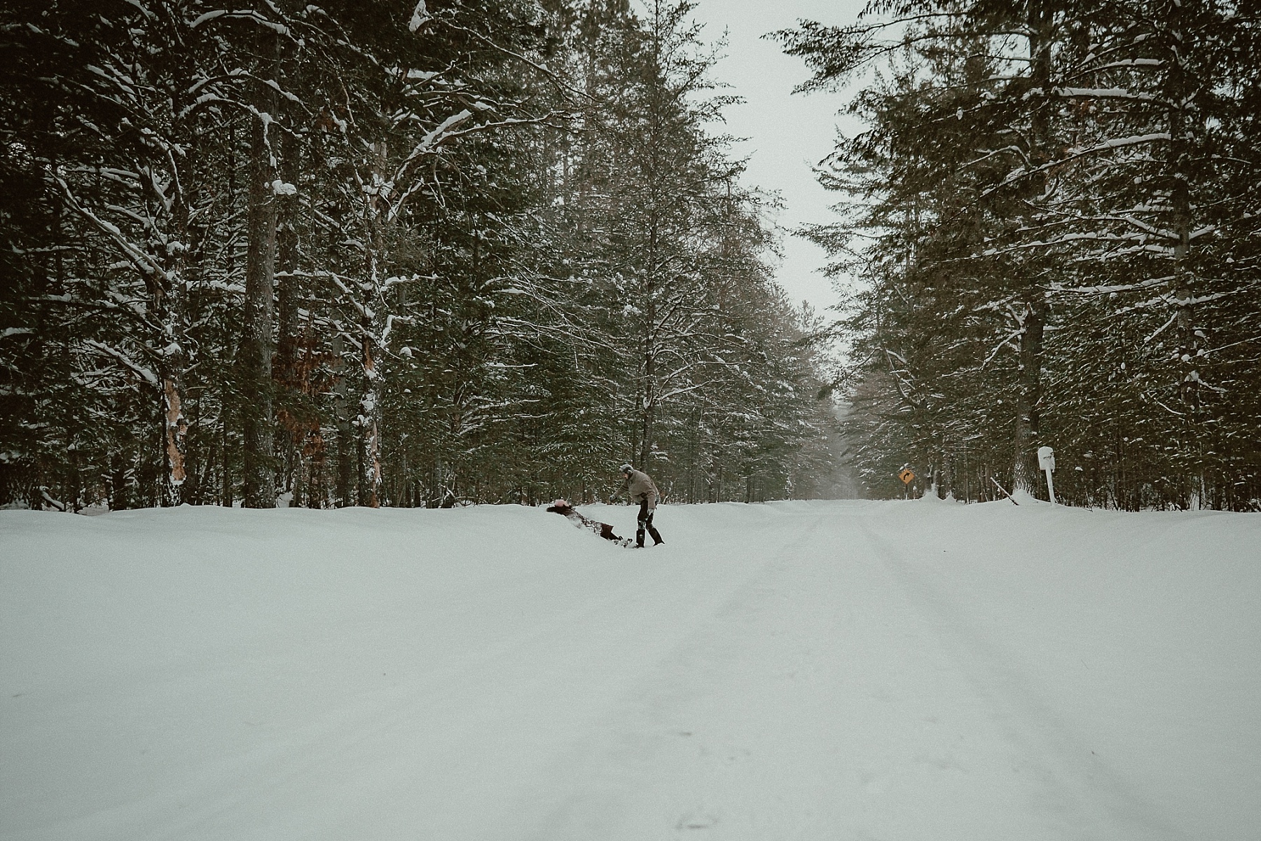 Him playfully pushing her into the snow bank during winter engagement session at Hartwick Pines State Park in Northern Michigan.