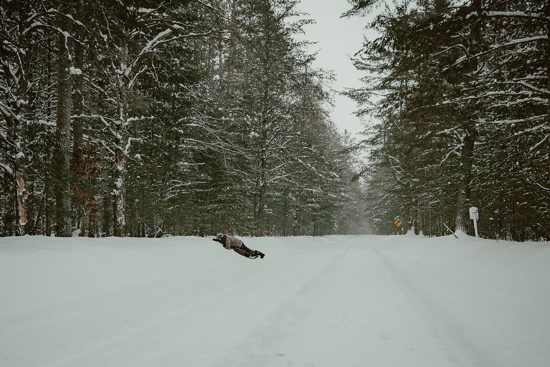 Couple laying in the snow kissing during winter engagement session at Hartwick Pines State Park in Northern Michigan.