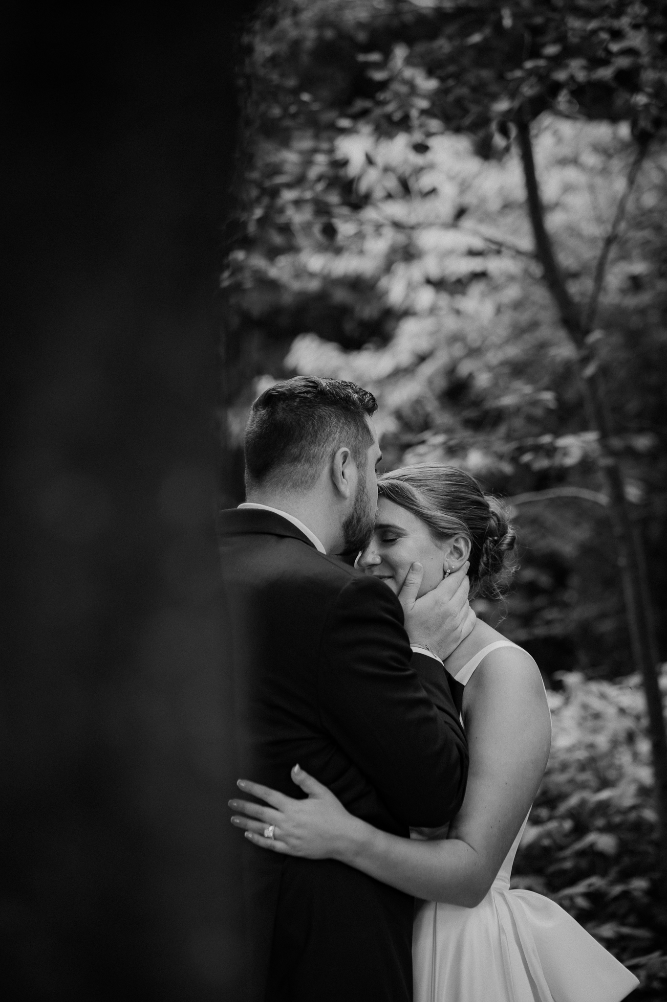 The groom holding his bride and kissing her forehead gently.
